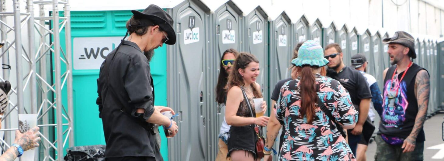 Groupe de festivaliers devant une rangée de toilettes mobiles WC Loc lors d’un événement en plein air.