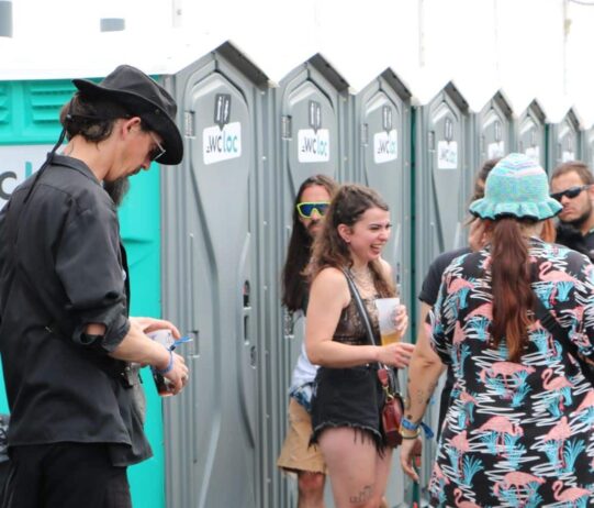 Groupe de festivaliers devant une rangée de toilettes mobiles WC Loc lors d’un événement en plein air.