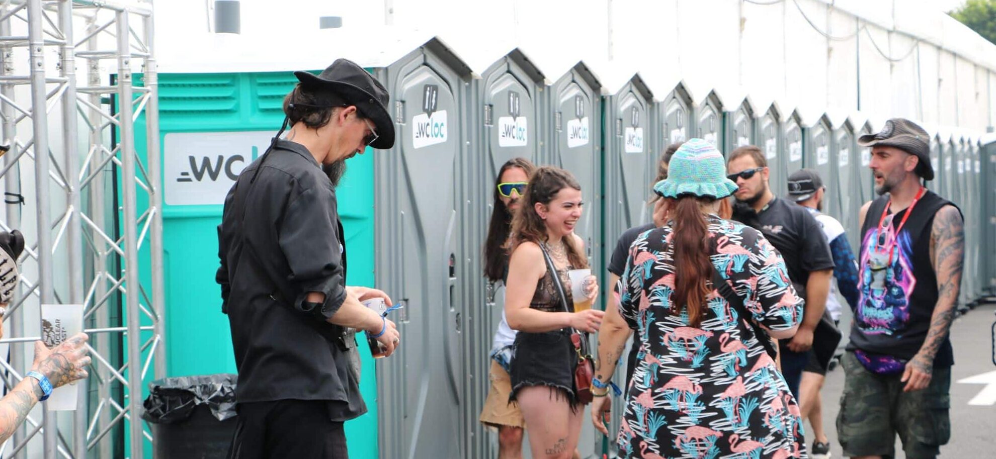 Groupe de festivaliers devant une rangée de toilettes mobiles WC Loc lors d’un événement en plein air.