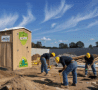 Toilette sèche de chantier avec urinoir, installée sur un site en construction, à côté de trois ouvriers en plein travail.