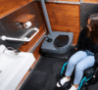 Femme en fauteuil roulant utilisant l’intérieur spacieux de la cabine WC Loc City Famille & PMR, équipée d’une barre d’appui, d’un lavabo accessible et d’un WC adapté.