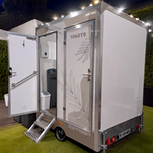 Caravane sanitaire mobile ouverte, avec accès par marche, lave-mains intégré et porte décorée de motifs floraux.