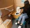 Personne en fauteuil roulant a l'intérieur de la cabine toilette sèche PMR