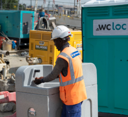 Un ouvrier de chantier portant un casque et un gilet de sécurité utilise un lavabo mobile pour se laver les mains sur le chantier