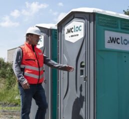 Opérateur sur un chantier utilisant une cabine WC Loc, illustrant la nécessité d’un lave-mains mobile pour garantir l’hygiène des travailleurs.