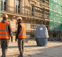 Deux compagnons en gilet orange discutent devant un urinoir autonome WC Loc sur un chantier de rénovation urbaine